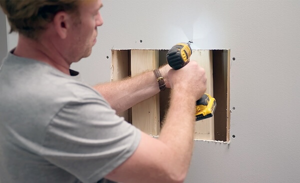 man repairing large hole in drywall with wood slats